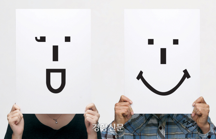 문자와 기호로 표현한 표정 이모티콘이 그려진 종이로 얼굴을 가리고 있는 모습. / 경향신문 자료사진