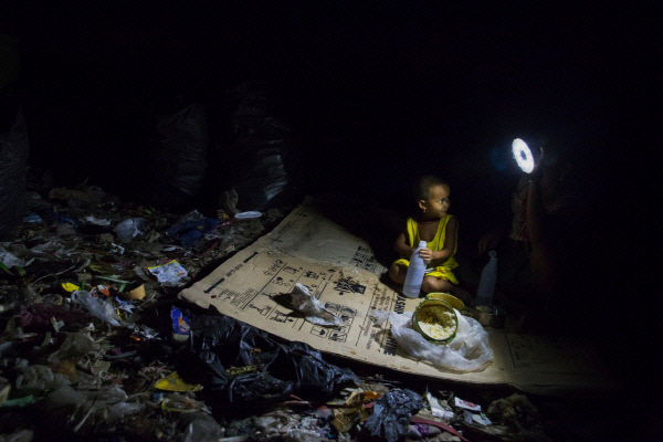 2017년 8월 태국 매솟의 쓰레기처리장에서 한 카렌족 아이가 종이 돗자리 위에 앉아 엄마를 쳐다보고 있다. |장준희 다큐멘터리 사진가