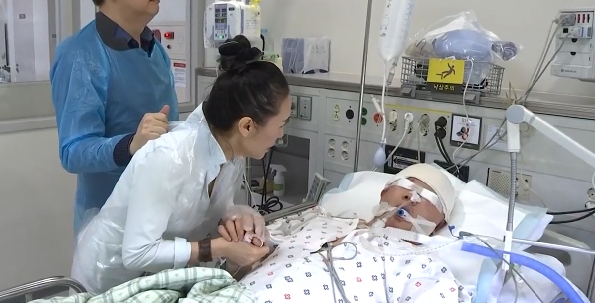 지난달 25일 부산에서 음주운전 차에 치어 아직까지 의식을 회복하지 못한 윤창호(22)씨. 가족들이 부산 해운대백병원 중환자실에 입원해 있는 그의 손을 꼭 잡고 회복을 기원하고 있다. JTBC ‘뉴스룸’ 방송화면 캡처