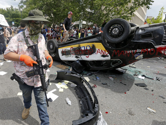 총기 들고 전복된 경찰차 옆을 지나는 ‘흑인 사망’ 시위대 - 미국 유타주 솔트레이크 시티의 도심에 30일(현지시간) 흑인 남성 조지 플로이드가 백인 경찰의 가혹 행위로 숨진 사건에 항의하는 시위대 수쳔명이 집결한 가운데 총기로 무장한 한 시위 참가자가 전복된 경찰 차량 옆을 지나고 있다. 솔트레이크시티 AP=연합뉴스    2020-05-31 14:34:26/