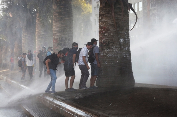 (사진출처=EPA/ELVIS GONZALEZ/연합뉴스)물대포를 피해 나무 뒤에 숨은 시위자들