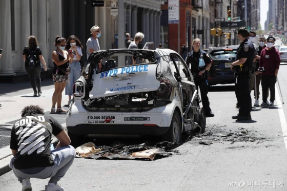 [뉴욕=AP/뉴시스]5월 31일(현지시간) 미국 뉴욕에서 플로이드 사망 항의 시위 중 불에 탄 뉴욕시 경찰 차량 주변에 경관 두 명이 서 있는 가운데 시민들이 이를 구경하고 있다. 지난달 25일 미니애폴리스 경찰관의 과잉 진압으로 숨진 흑인 남성 조지 플로이드의 죽음을 두고 미국 곳곳에서 시위가 벌어지고 있다. 2020.06.01.