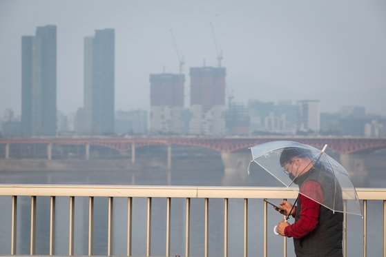 수도권 미세먼지 비상저감조치가 엿새째 이어진 지난 3월 6일 서울 동호대교 남단에서 마스크를 착용한 시민이 우산을 쓰고 걸어가고 있다. [뉴스1]