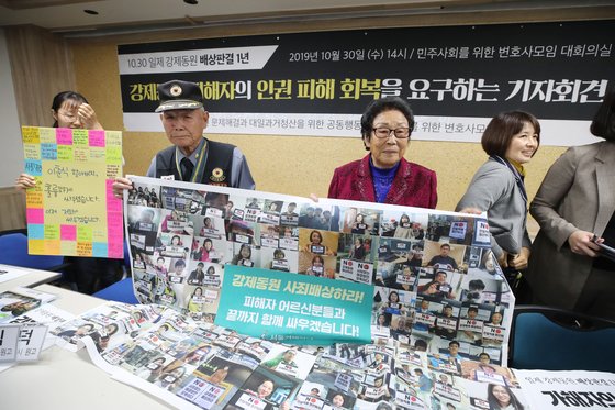 일제강제동원 피해자 이춘식 할아버지와 양금덕 할머니가 30일 오후 서울 서초구 민변 대회의실에서 열린 '일제강제동원 배상판결 1년, 피해자 인권 피해 회복 요구 기자회견'에 참석해 겨레하나 회원들, 재일동포 등의 응원 문구와 현수막을 들고 기념촬영하고 있다. [연합뉴스]
