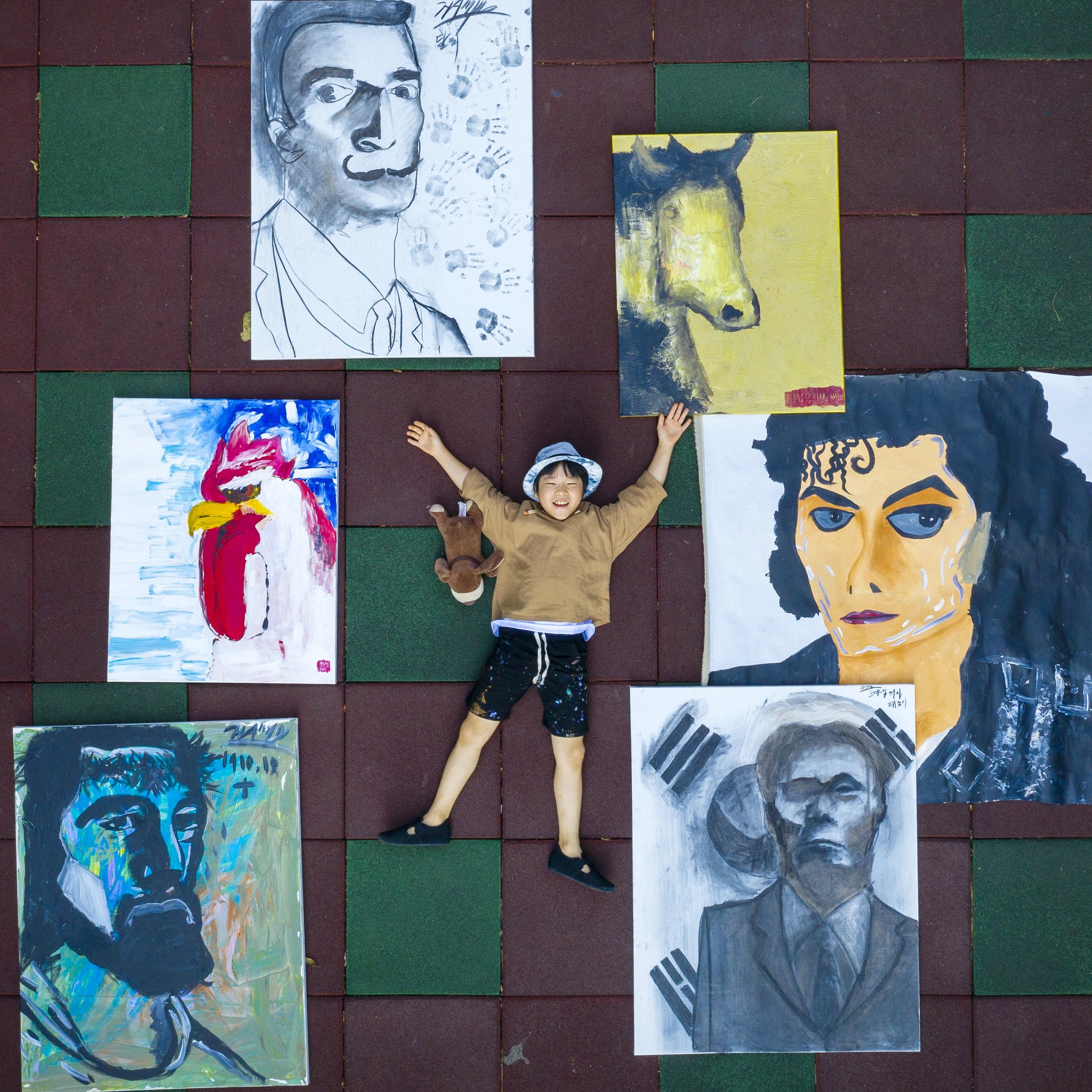 '꼬마 피카소' 김하민군이 자신이 그린 좋아하는 그림들과 함께 누웠다. 왼쪽 아래부터 예수 그리스도, 집에서 키웠던 닭을 그렸다. 살바도르 달리, 황소를 닮은 백마 우리를 본다, 마이클 잭슨, 윤봉길 의사. 하민이의 곁에는 가장 좋아하는 인형 '강순이'도 함께 했다. 장진영 기자