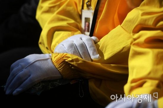 노란 옷을 입은 어머니가 철거가 진행 중인 광장을 바라보고 있다. 나란히 모은 두 손 뒤로 목에 걸린 학생증이 보인다. /문호남 기자 munonam@