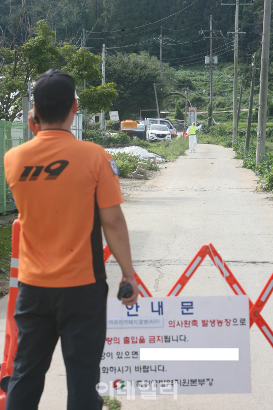 아프리카돼지열병이 발생한 파주 연다산동의 양돈농가와 약 100m 떨어진 곳에 차단기가 설치돼 현장에 물 공급을 위해 출동한 소방대원이 방역당국 관계자와 연락을 시도하고 있다.(사진=정재훈기자)