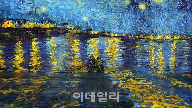 ‘빛의 벙커’에서 투사한 빈센트 반 고흐의 ‘아를의 별이 빛나는 밤’(1888)을 정면에서 바라봤다. 연인으로 보이는 저 남녀는 원작에선 강변을 따라 산책 중이었다(사진=오현주 문화전문기자).