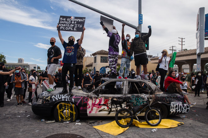 30일(현지시간) 미국 로스엔젤레스(LA)에서 백인 경찰에게 목을 눌려 숨진 흑인 조지 플로이드를 추모하기 위해 모인 시위대가 경찰차를 전복시킨 뒤 차량 위에 올라가 항의 시위를 하고 있다. (사진=AFP)