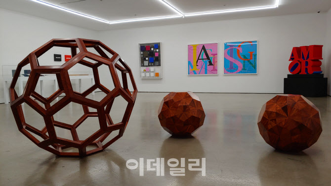 갤러리현대 50주년 특별전 ‘현대 50’ 후반부 전시 전경. 아이 웨이웨이가 반려묘의 플라스틱 장난감을 중국 장인의 전통 가구생산방식으로 재탄생시킨 나무조각 ‘F 사이즈’(2011)와 ‘무제’(2010) 뒤로, 오른쪽부터 로버트 인디애나의 ‘AMOR’(1998), 마이클 크레이그 마틴의 ‘무제’(2010) 두 점, 헤수스 라파엘 소토의 ‘양면성-11’(1981) 등이 보인다(사진=오현주 문화전문기자).