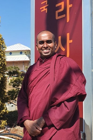 (아산=연합뉴스) 이희용 기자 = 담마끼띠 스님이 마하위하라사원 입간판 앞에서 포즈를 취하고 있다. 뒤로 법당 건물이 보인다.