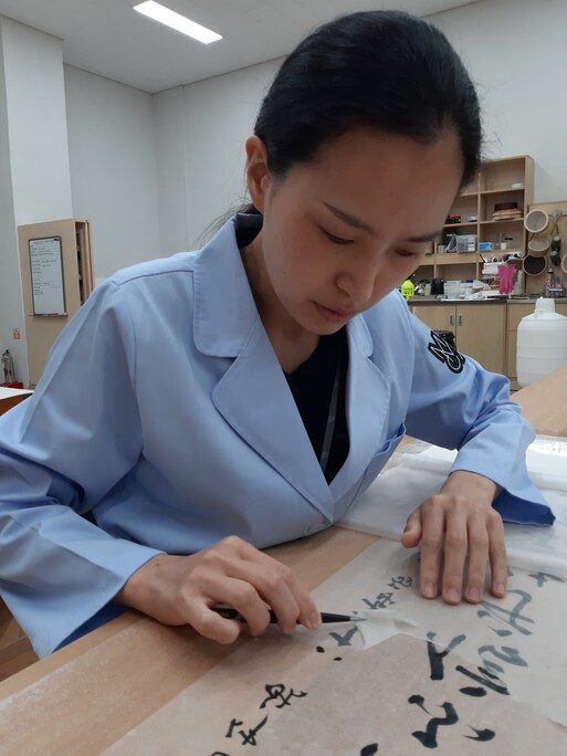 이병도 서예가의 글씨 작품을 놓고 작품 뒤의 묵은 배접지를 벗기는 지류실 김미나 학예사의 작업 모습. 높은 집중도와 긴장이 요구되는 작업이다.