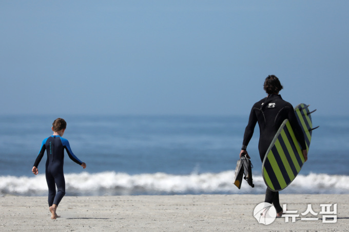 [롱아일랜드 로이터=뉴스핌] 김민정 기자 = 22일(현지시간) 메모리얼 데이 연휴를 맞아 개방된 미국 뉴욕 롱아일랜드 롱비치에서 한 남성이 아이와 서핑보드를 들고 걷고 있다.  2020.05.23 mj72284@newspim.com