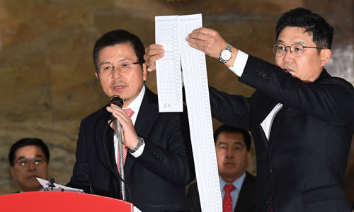 “정당 난립… 투표용지 1.3m” 자유한국당 황교안 대표(왼쪽)가 23일 국회 로텐더홀에서 열린 당 최고위원회의에서 “연동형 비례대표제를 도입하면 약 100개 정당이 난립할 수 있고 정당투표용지 길이가 1.3m에 달할 수 있다”고 비판하자 성동규 여의도연구소장이 가상의 투표용지를 들어보이고 있다. 허정호 선임기자